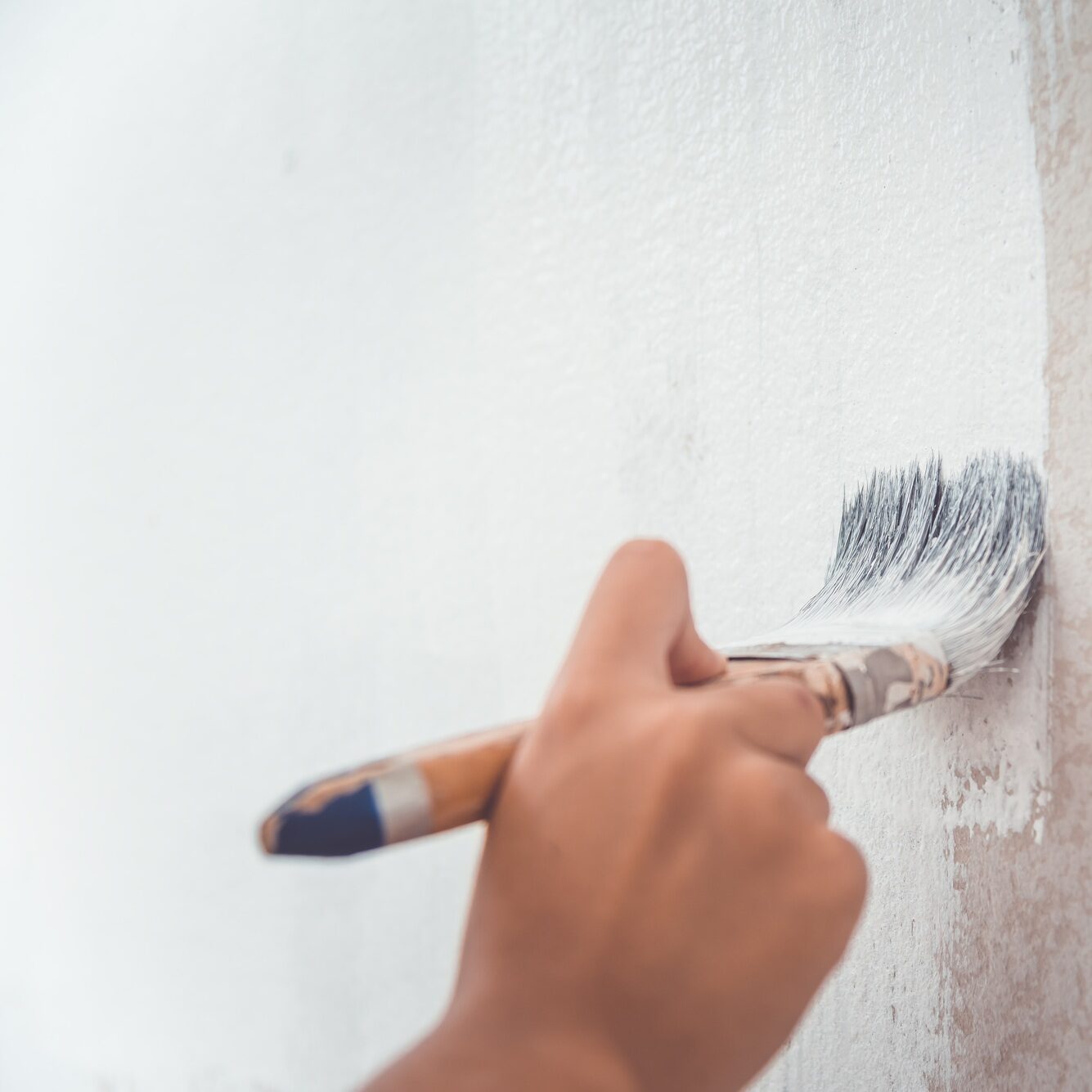 hand was holding a brush to paint the wall using white paint.