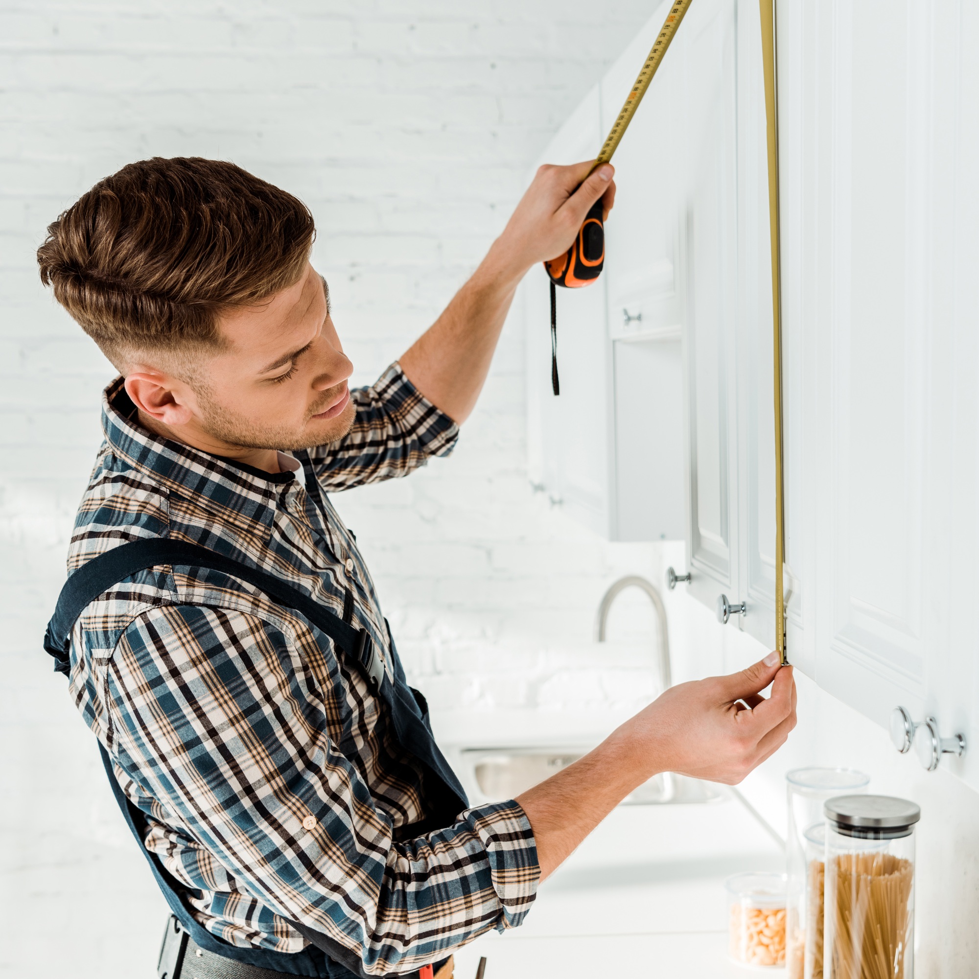 handsome installer measuring white kitchen cabinet